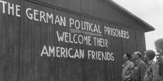 Soldiers of the 46th Armored Infantry, 5th Armored Division, U.S. Ninth Army, and their guide read, "THE GERMAN POLITICAL PRISONERS WELCOME THEIR AMERICAN FRIENDS," painted on the outside wall of one of the barracks of the political prisoners at the Buchenwald concentration camp, near Weimar, Germany. May 1945. 