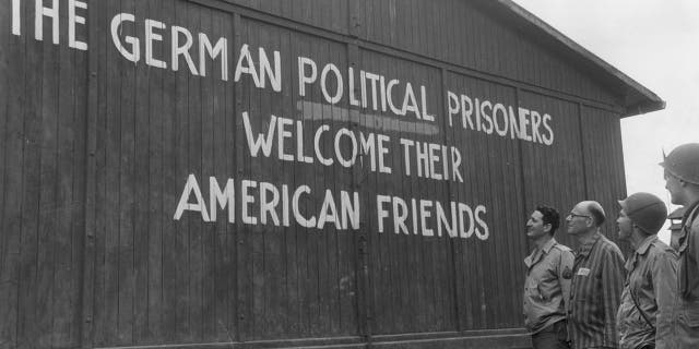 Soldiers of the 46th Armored Infantry, 5th Armored Division, U.S. Ninth Army, and their guide read, "THE GERMAN POLITICAL PRISONERS WELCOME THEIR AMERICAN FRIENDS," painted on the outside wall of one of the barracks of the political prisoners at the Buchenwald concentration camp, near Weimar, Germany. May 1945. 