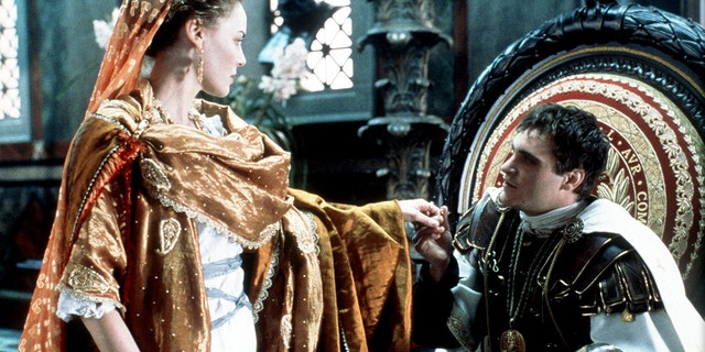 Joaquin Phoenix sits on a throne and holds the hand of Connie Nielsen in a scene from "Gladiator"