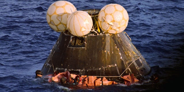 Navy swimmers fasten a floatation collar around the Apollo 13 capsule as it floats after splashdown in the Pacific Ocean. Aboard are James Lovell, John Swigert, and Fred Haise.