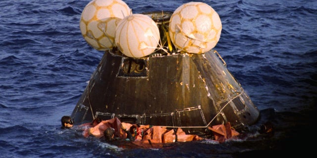 Navy swimmers fasten a floatation collar around the Apollo 13 capsule as it floats after splashdown in the Pacific Ocean. Aboard are James Lovell, John Swigert, and Fred Haise.