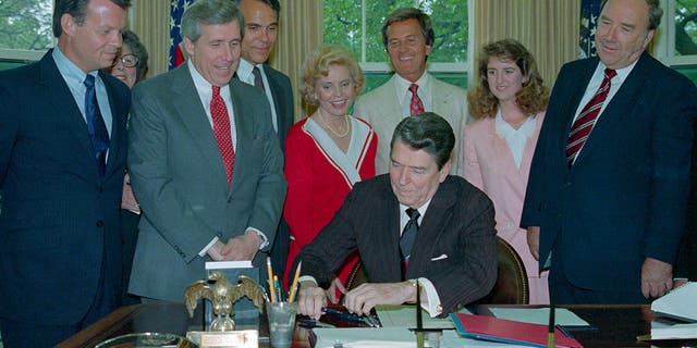 Members of the National day Prayer organizing committee looking on, including entertainer Pat Boone, (C-white suit), President Reagan signs a proclamation honoring the day in an oval office ceremony May 5th.