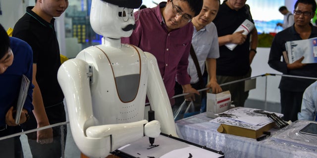 Onlookers watch a robot painting in Shenzhen, China, Nov. 16, 2017.