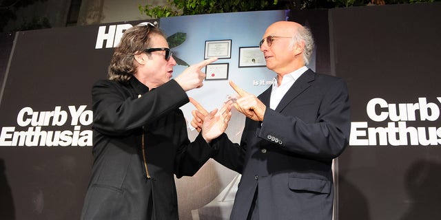 Richard Lewis and Larry David laughing and pointing at each other on the red carpet