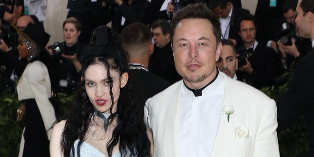 Elon Musk in a white tuxedo and Grimes in a white dress and black accents on the Met Gala red carpet 