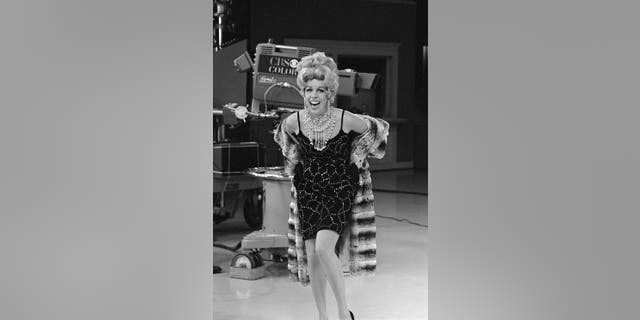 Carol Burnett in a glitzy costume standing next to a camera