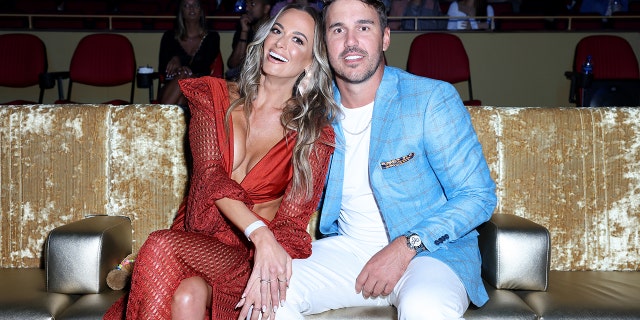 Jena Sims in a low-cut red dress next to Brooks in a white shirt and pants with a bright blue leather jacket