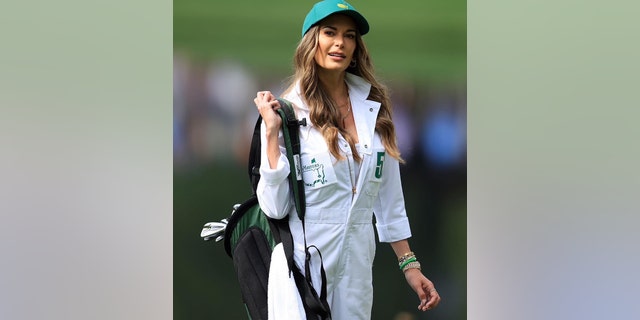 Jena Sims in a white caddy uniform holding golf clubs
