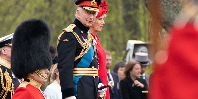 King Charles in a military uniform next to Queen Camilla in a red dress with a matching hat