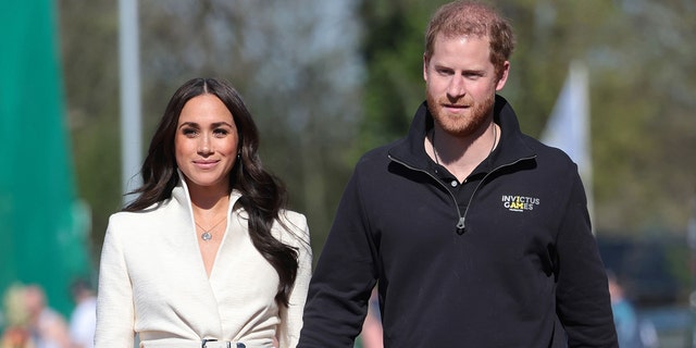 Meghan Markle in a beige top walking next to Prince Harry wearing a black sweater