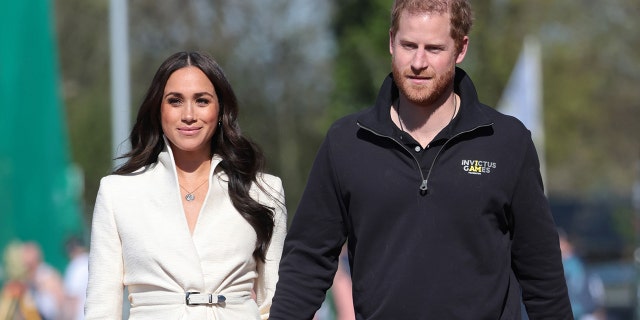 Meghan Markle in a beige top walking next to Prince Harry wearing a black sweater