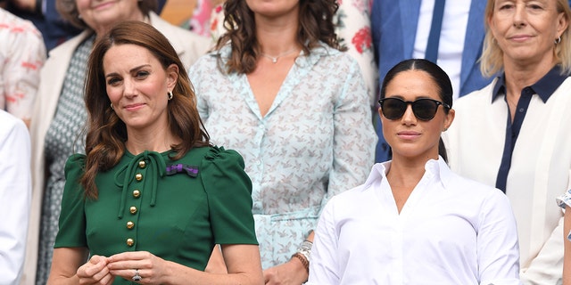Kate Middleton wearing a green dress next to Meghan Markle wearing a white blouse and sunglasses