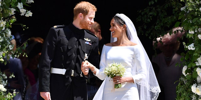 Meghan Markle wearing a white bridal dress holding Prince Harrys hand, who is wearing a suit