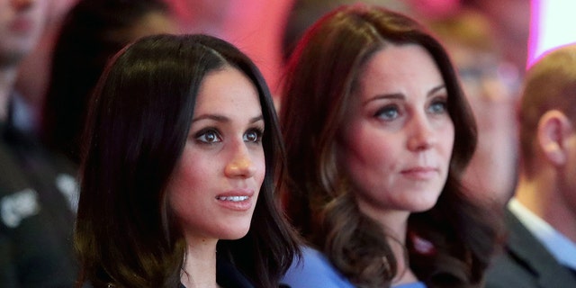 A side photo of Meghan Markle wearing a dark hued dress next to Kate Middleton wearing a blue dress
