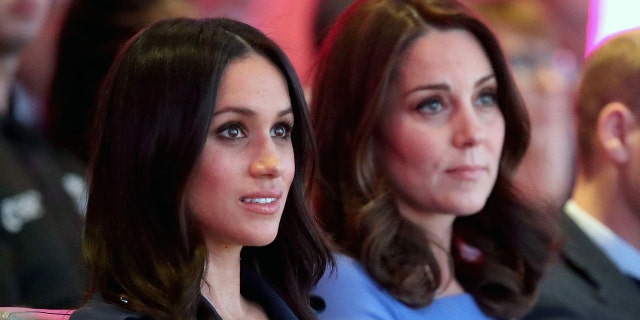 A side photo of Meghan Markle wearing a dark hued dress next to Kate Middleton wearing a blue dress