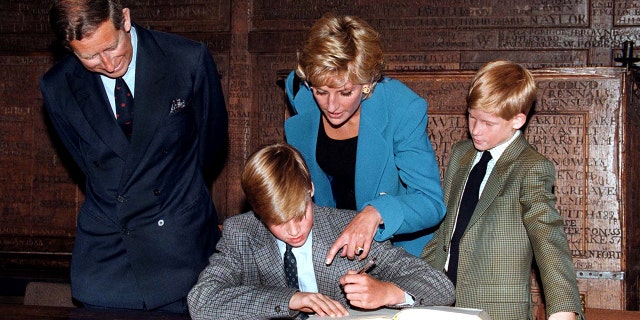 Princess Diana pointing at Prince Williams book while Prince Harry and Prince Charles watch on