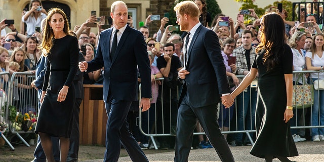 Prince William and Catherine, the new Prince and Princess of Wales, accompanied by Prince Harry and Meghan, the Duke and Duchess of Sussex wearing black walking towards a crowd