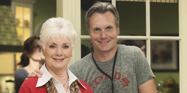 Ryan Cassidy in a grey shirt next to his mother Shirley Jones in a white collared blouse and a red blazer with a yellow patterned scarf