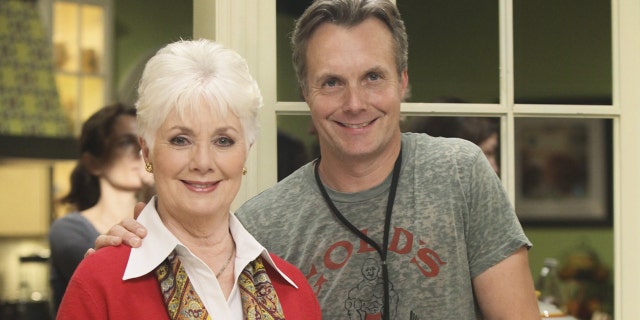 Ryan Cassidy in a grey shirt next to his mother Shirley Jones in a white collared blouse and a red blazer with a yellow patterned scarf