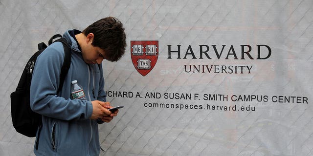 A man looks at his cell phone near the Harvard University sign in Cambridge, Massachusetts, US, June 18, 2018.  REUTERS/Brian Snyder