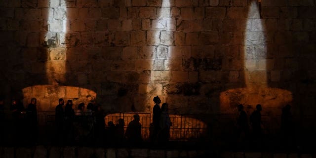 People walk by an image of memorial candles, projected on the walls of Jerusalem's Old City on the eve of annual Holocaust Remembrance Day on April 17, 2023.
