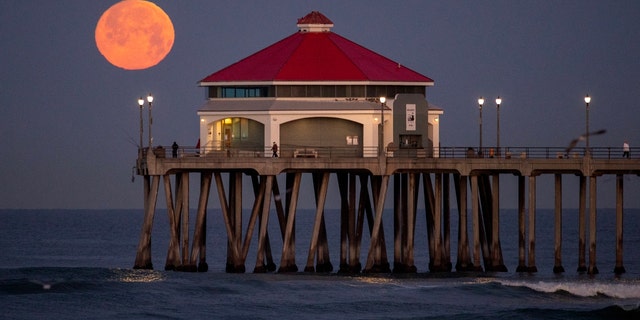 Fishermen and pier walkers have a scenic view of the setting full pink moon, named after blooming wildflowers, at dawn at the Huntington Beach Pier in Huntington Beach, California, Wednesday, April 5, 2023. 