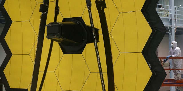 A technician stands next to the James Webb Space Telescope