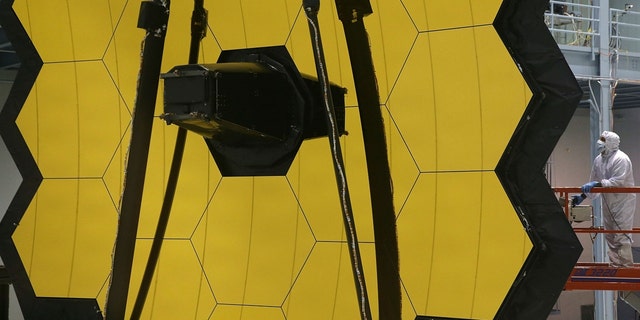 A technician stands next to the James Webb Space Telescope