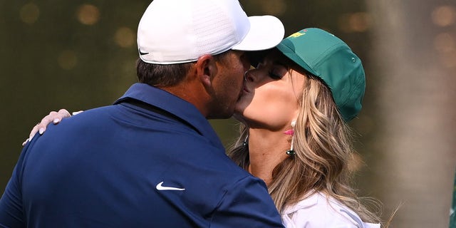 Brooks Koepka of the United States kisses his wife, Jena Sims Koepka, on the ninth green during the Par 3 contest ahead of the 2023 Masters Tournament at Augusta National Golf Club on April 5, 2023 in Augusta, Georgia.