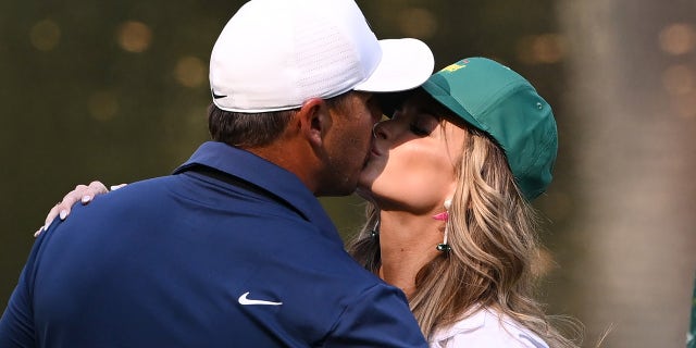 Brooks Koepka of the United States kisses his wife, Jena Sims Koepka, on the ninth green during the Par 3 contest prior to the 2023 Masters Tournament at Augusta National Golf Club on April 05, 2023 in Augusta, Georgia.
