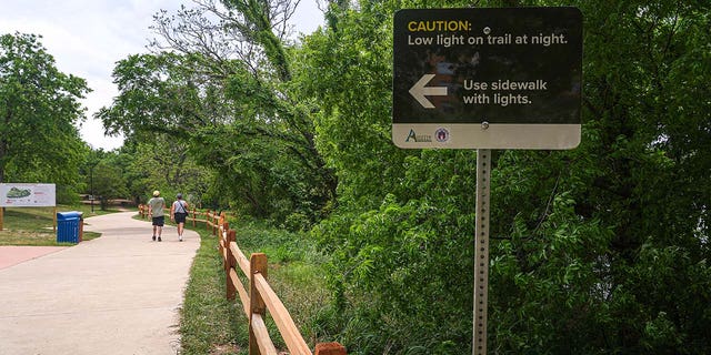 A sign warns of poor lighting conditions at night on a hike and bike trail along Lady Bird Lake