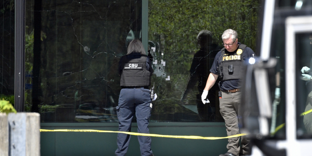 A Louisville Metro Police crime scene technician photographs bullet holes in the glass of the Old National Bank building in Louisville on Monday, April 10.