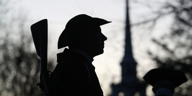 A Lexington Minuteman waits on Lexington Common, in the pre-dawn hour. The Battle of Lexington is commemorated on Patriots' Day, April 18, 2022, in Lexington, Massachusetts. The town pays tribute to those who died on the morning of April 19, 1775.