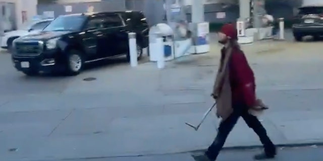 Man in ragged clothes carrying pipe down street