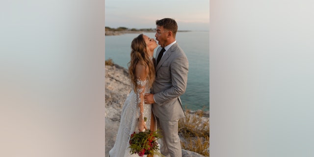 Jena Sims se inclina para darle un beso con su vestido de novia mientras Brooks Koepka hace una mueca con un traje gris.