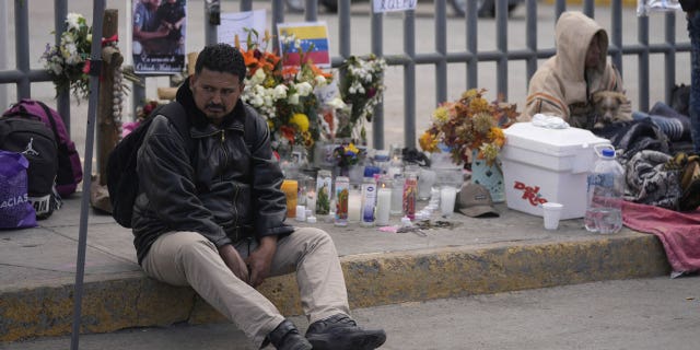 A Venezuelan migrant sits on the sidewalk where an altar was created with candles and photos outside the Mexican immigration detention center in Ciudad Juarez, Mexico, on March 30, 2023.