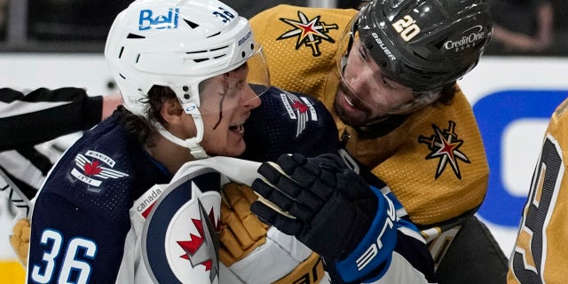 Vegas Golden Knights center Chandler Stephenson, #20, helps Winnipeg Jets center Morgan Barron, #36, after Barron cut his face on a skate during the first period of Game 1 of an NHL hockey Stanley Cup first-round playoff series Tuesday, April 18, 2023, in Las Vegas.