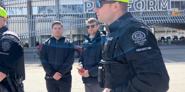 Nathaniel Pawlowski, second from right, holds a Bible and stands with friend Deklan Friesen as officers detain them.