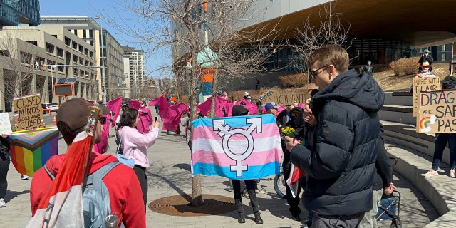 Nathaniel Pawlowski reads the Bible outside the Calgary Public Library as protesters demonstrate with placards and a trans flag.