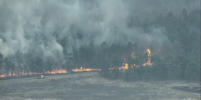 A truck drives on a road surrounded by flames and smoke from the Jimmy's Waterhole Fire