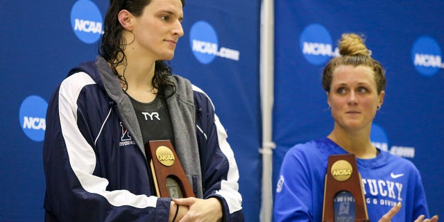 Penn Quakers swimmer Lia Thomas holds a trophy after finishing fifth in the 200 free at the NCAA Swimming &amp; Diving Championships as Kentucky Wildcats swimmer Riley Gaines looks on at Georgia Tech.