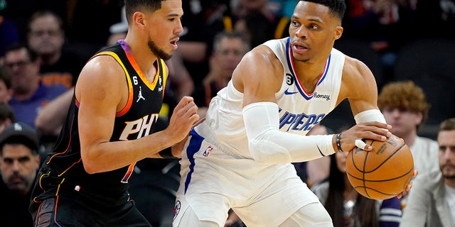 El escolta de Los Angeles Clippers, Russell Westbrook, retira al escolta de los Phoenix Suns, Devin Booker, a la izquierda, durante la segunda mitad del Juego 1 de una serie de playoffs de baloncesto de la NBA en la primera ronda, el domingo 16 de abril de 2023, en Phoenix.