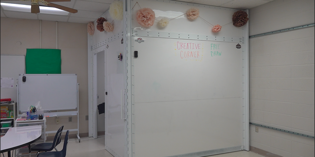 The bulletproof shelter stands in the corner of a teacher's classroom. From the outside, it looks like a dry-erase board.