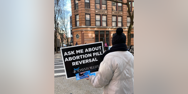 A pro-life advocate holds a sign about reversing the abortion pill.