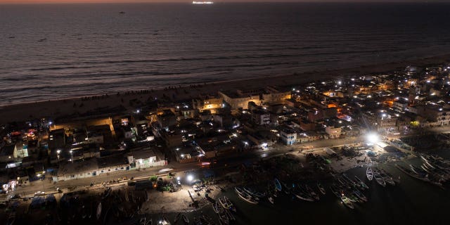 An offshore gas terminal is lit up amid the Atlantic Ocean as houses lay on the beachfront between the sea and the Senegal River, bottom, in Saint Louis, Senegal, on Jan. 18, 2023.