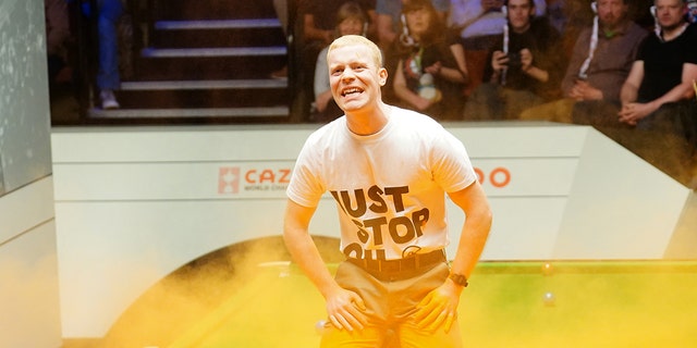 Un manifestante de Just Stop Oil salta sobre la mesa y arroja polvo naranja durante el partido entre Robert Milkins v Joe Perry el tercer día del Campeonato Mundial de Snooker Cazoo en el Teatro Crucible en Sheffield.  Imagen fecha: lunes 17 de abril de 2023.