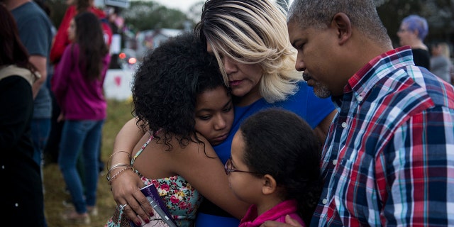FILE - Tabitha and Jalaina embrace next to Brad and Jacera as they listen to dozens of people standing in the rain pray and sing together at the memorial crosses near the Sutherland Springs First Baptist Church one week after 26 people were killed inside in Sutherland Springs, Texas on November 12, 2017. The family, who withheld their last name, came from North Carolina to support the community.