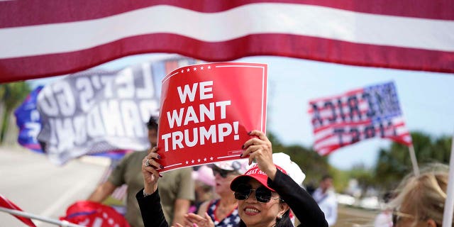 Supporters of former President Donald Trump hold signs and wave flags in support of Trump outside Trump International Golf Club