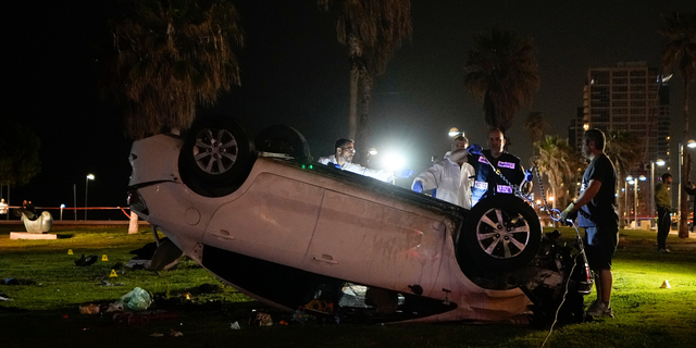 Israeli police stand around a car involved in an attack in Tel Aviv, Israel, Friday, April 7, 2023. Israeli police said a car rammed into a group of people near a popular seaside park before flipping over. Police said they shot the driver of the car. Israel's rescue service described the incident as a shooting attack.