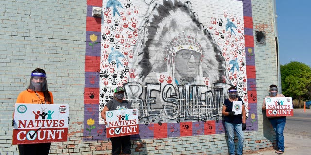 Activists hold signs promoting Native American participation in the U.S. census in front of a mural of Crow Tribe historian Joe Medicine Crow in Montana on Aug. 26, 2020. A judge in Montana refused to dismiss a lawsuit alleging that the state constitution’s Native American education requirements have not been upheld.